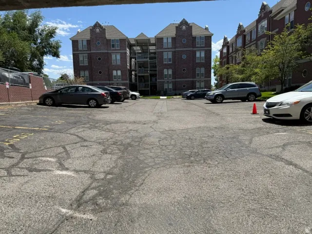 Paved parking area for multi-story residential buildings featuring brick exteriors, gabled roofs, and mature trees