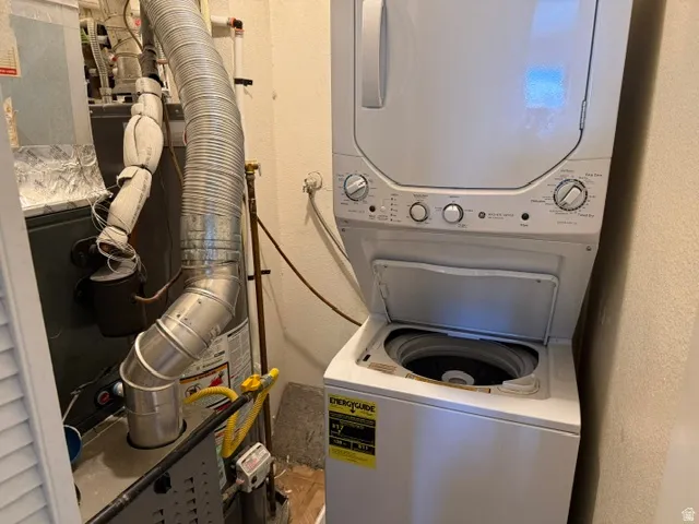 Stackable washer and dryer unit with top-load washer, utility connections, and adjacent HVAC system
