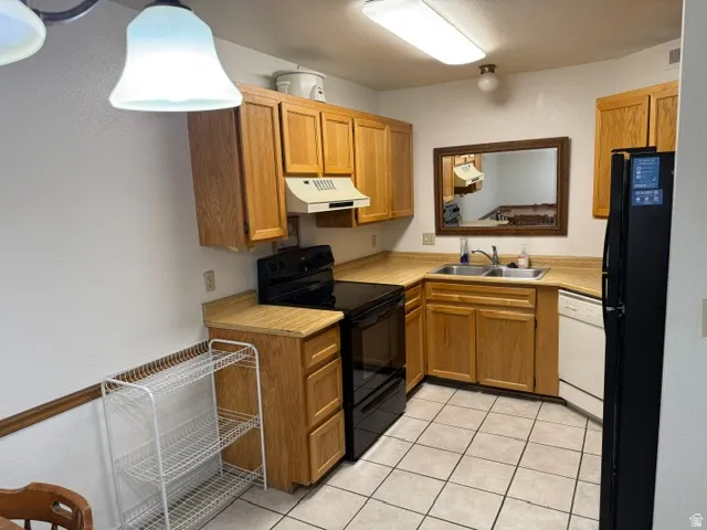 Kitchen featuring wood cabinetry, laminate countertops, a double-basin stainless steel sink, black range, and white tile flooring