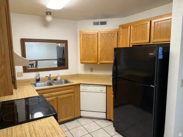 Kitchen featuring light wood cabinetry, laminate countertops, a double basin stainless steel sink, a black electric range, and a black refrigerator