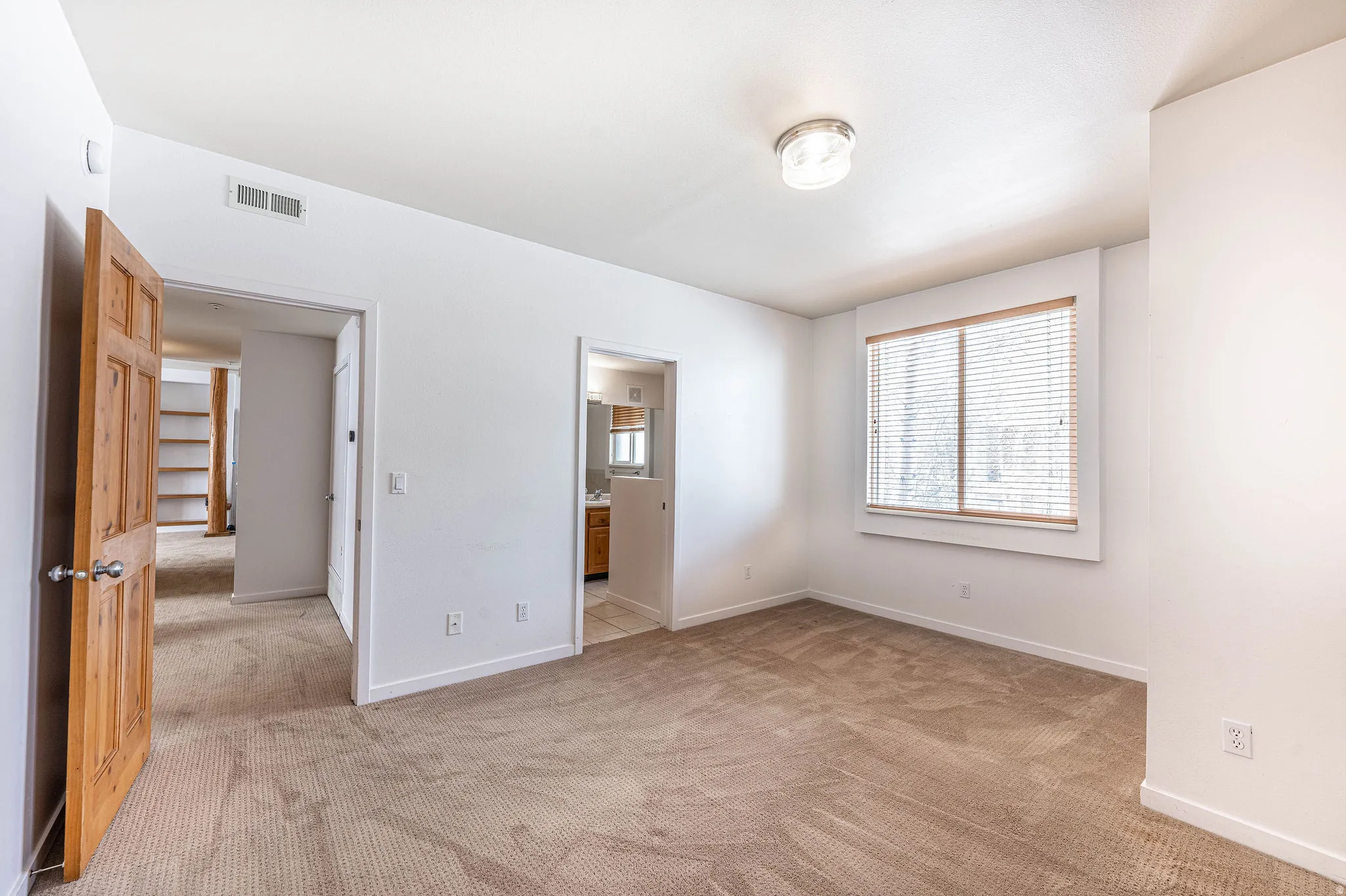 Carpeted room with a ceiling-mounted light fixture and a window featuring horizontal blinds