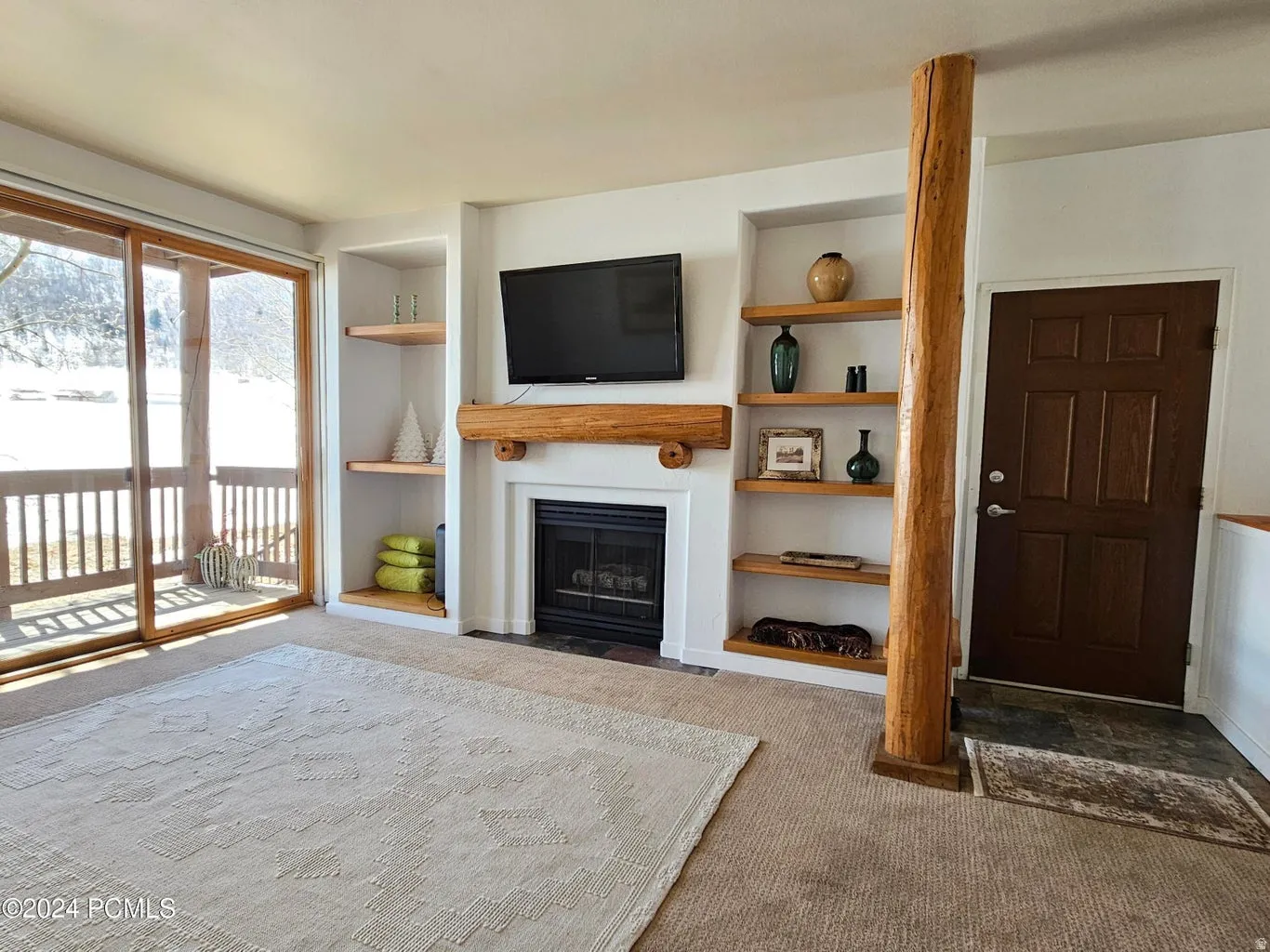 Living area featuring a central fireplace with an integrated mantel, built-in shelving, a natural wood-finish structural column, and sliding glass doors opening to an exterior balcony