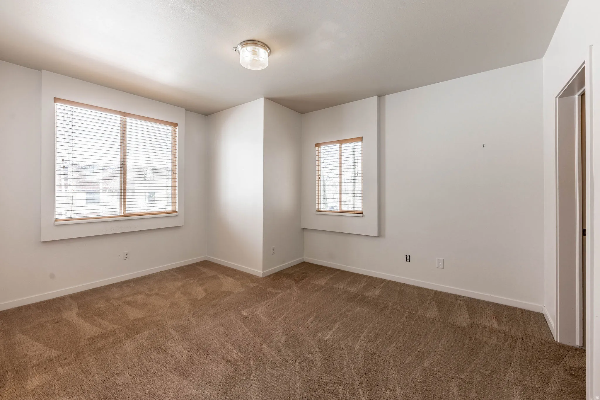 Carpeted room featuring multiple windows with blinds, a ceiling-mounted light fixture, and white painted walls