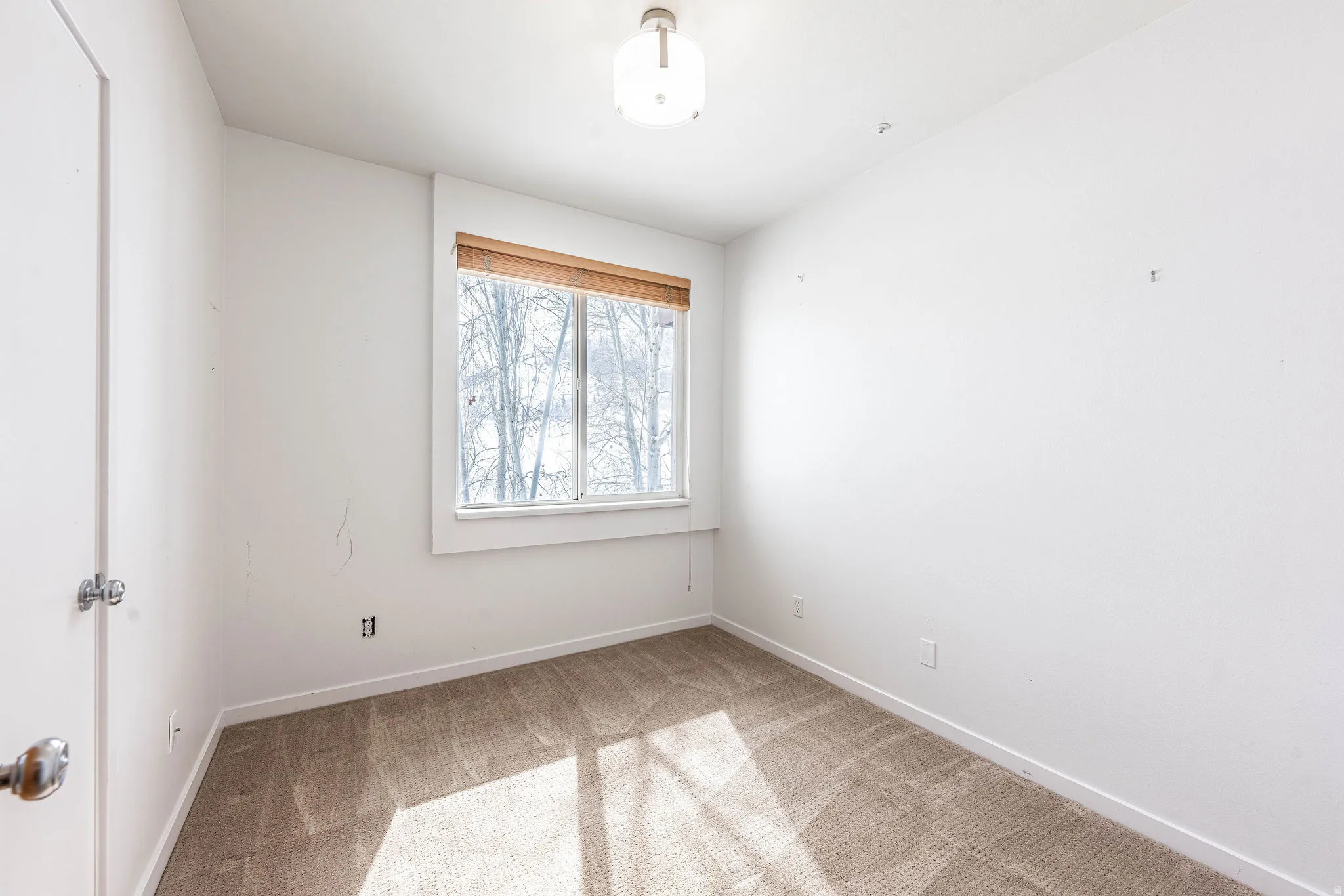 Carpeted room featuring a single window with a wood-finish blind, white trim, and a semi-flush mount ceiling light