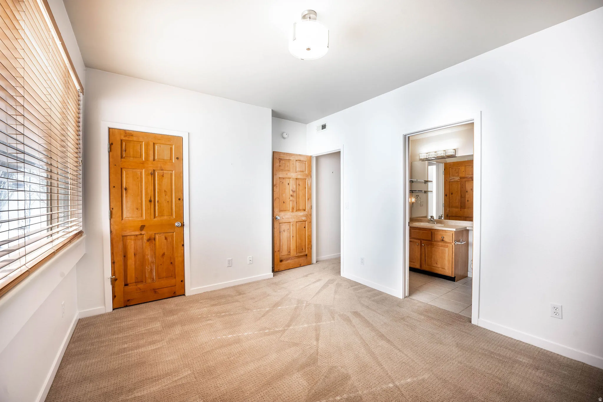 Spacious room featuring neutral carpet flooring, white walls, and natural wood doors
