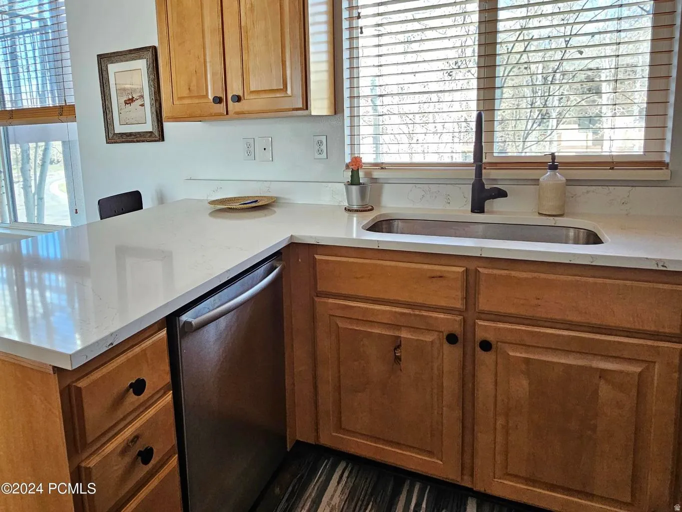 Kitchen featuring light wood cabinetry with black hardware, white countertops, and a built-in stainless steel dishwasher