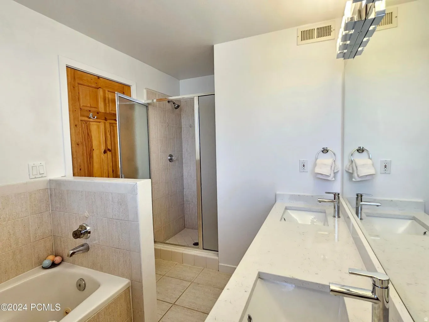 Contemporary bathroom featuring a double vanity with integrated sinks and chrome fixtures, a full-width mirror, a tiled shower enclosure with a glass door, and a built-in tub with coordinating tile surround