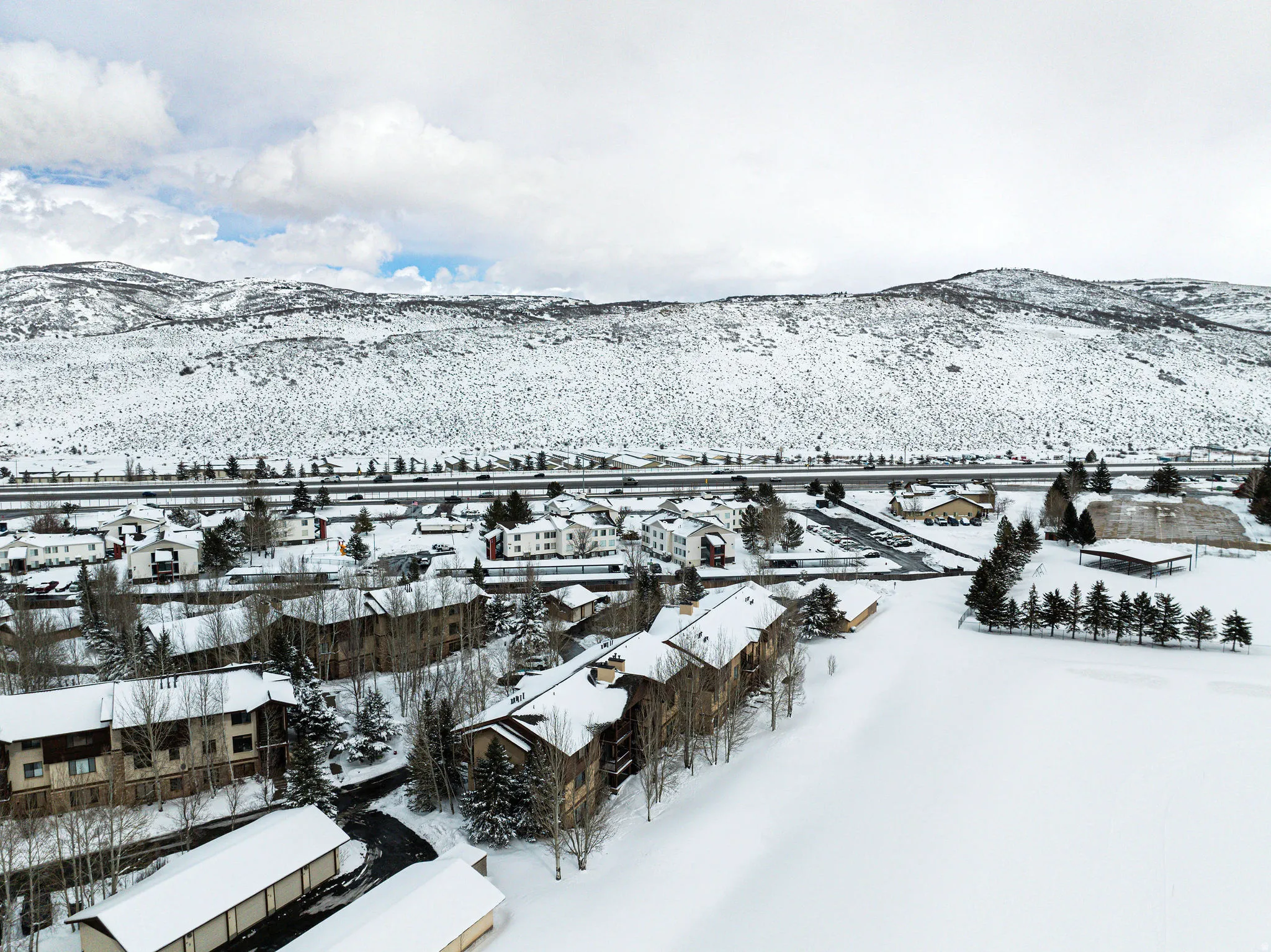 Community setting featuring multi-story residential buildings, snow-covered grounds, and a backdrop of snow-capped mountains