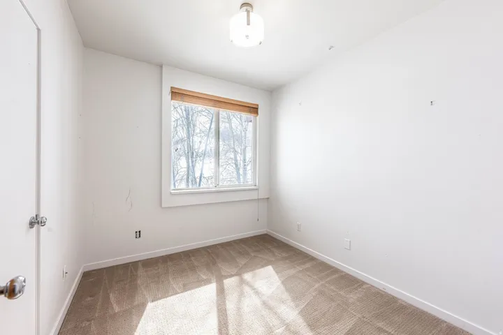 Carpeted room featuring a single window with a wood-finish blind, white trim, and a semi-flush mount ceiling light