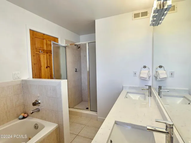 Contemporary bathroom featuring a double vanity with integrated sinks and chrome fixtures, a full-width mirror, a tiled shower enclosure with a glass door, and a built-in tub with coordinating tile surround
