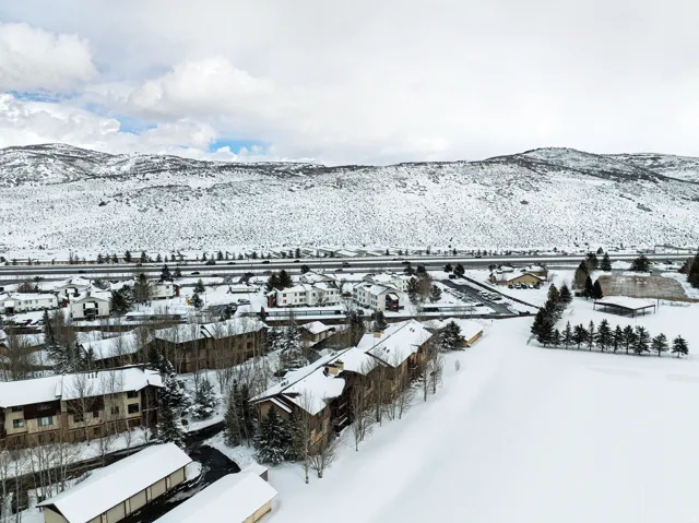 Community setting featuring multi-story residential buildings, snow-covered grounds, and a backdrop of snow-capped mountains