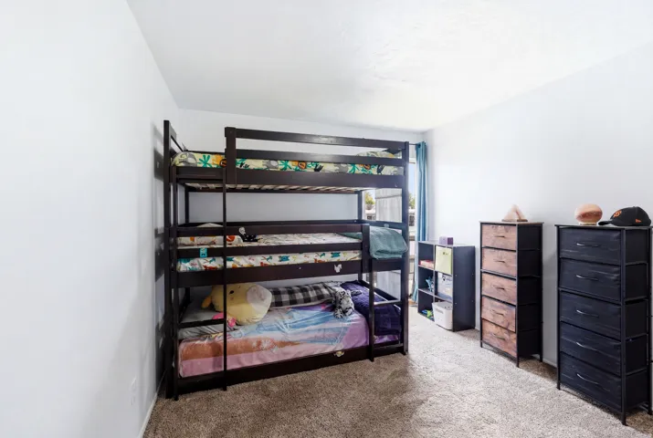 Carpeted room with a window featuring blue curtains, white walls, and a built-in shelf unit