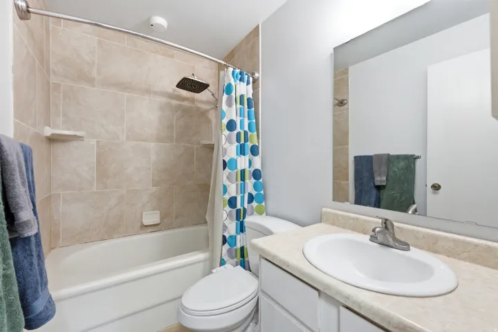 Bathroom featuring a white vanity with an integrated sink, a large wall-mounted mirror, and a full bathtub with a tiled surround and a rainfall showerhead