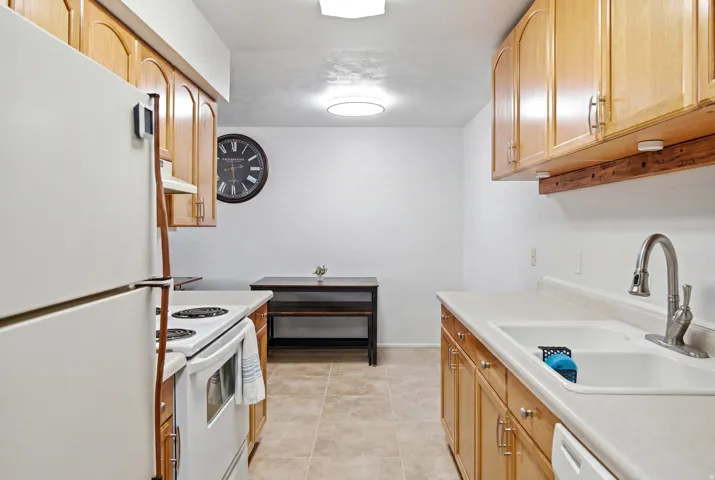 Well-appointed kitchen featuring light wood-finish cabinetry, white countertops, a double-basin sink with a gooseneck faucet, and tiled flooring