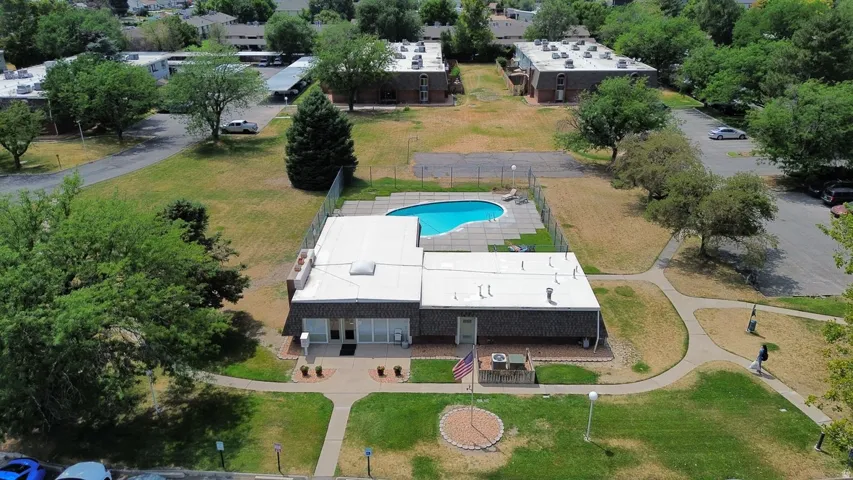 Community building featuring a swimming pool with surrounding patio, fenced pool area, manicured lawn, and paved walkways
