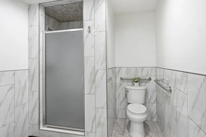 Shower stall with a frosted glass door, complemented by white and gray veined tile walls and flooring