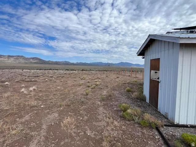 Expansive undeveloped acreage featuring a distant mountain range backdrop and a white corrugated metal outbuilding with a wood door