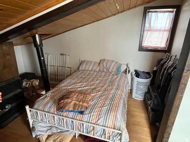 Sloped wood-finish ceiling featuring exposed beams, a built-in window with dark trim, wood-finish flooring, and a visible heater
