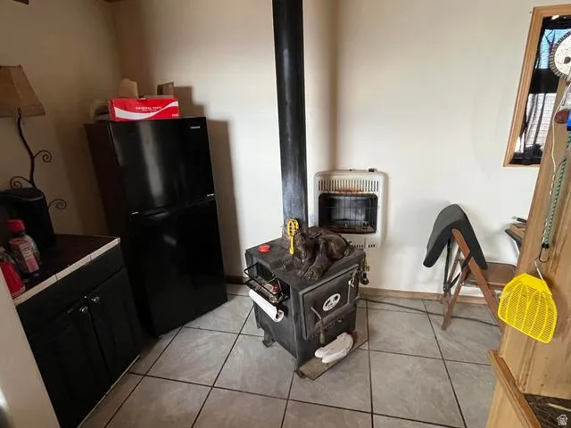 Room featuring a freestanding wood-burning stove with a stovepipe, wall-mounted heater, and tile flooring