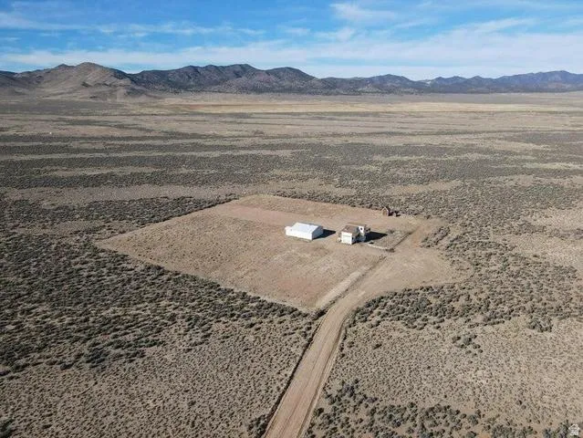 Expansive arid landscape featuring a detached residence, an auxiliary building, and a distant mountain range