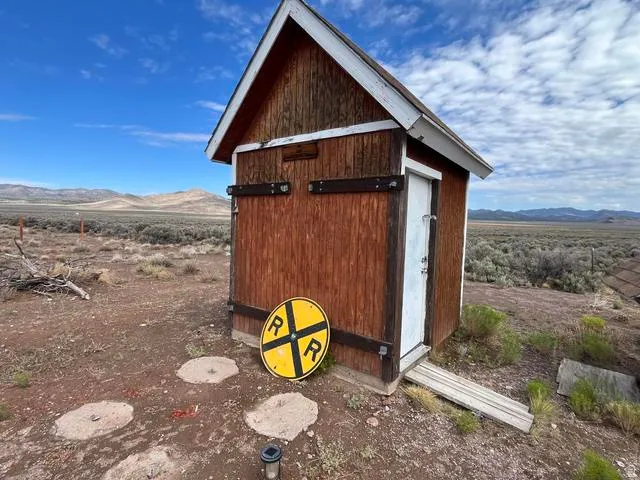 Compact wooden structure with a pitched roof, white door, and a small wooden ramp