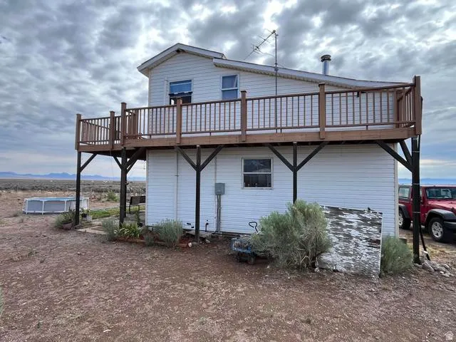 White siding exterior with a second-story wood-tone deck featuring a railing