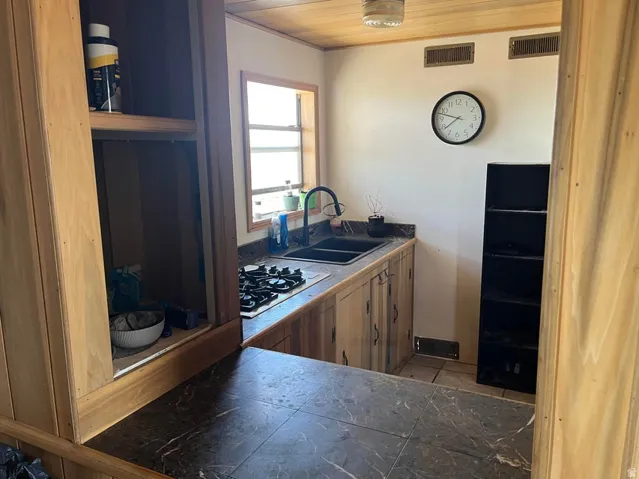 Warm wood-finish cabinetry with dark hardware, dark stone-finish countertops, and a black double basin sink with a gooseneck faucet