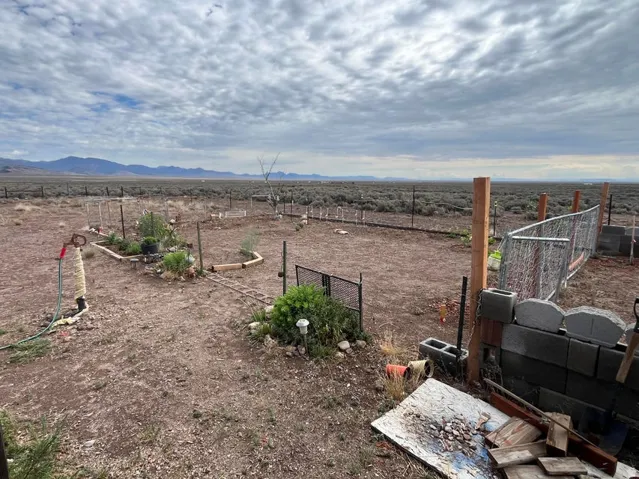 Expansive open land with a partial chain-link fence, wood fence posts, and distant mountain ranges
