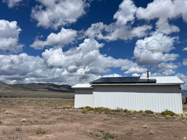 White corrugated metal siding, metal roof, solar panel array, and a remote mountain backdrop