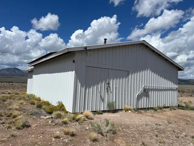 Corrugated metal siding structure with a gable roof, exterior lighting fixtures, a chimney, and a pipe railing