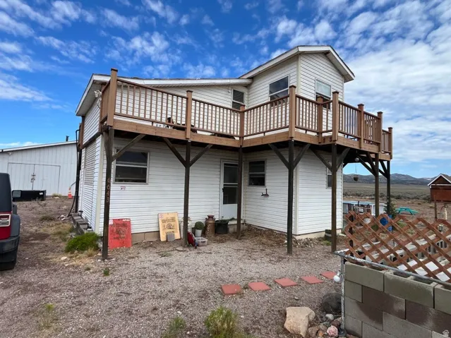 Multi-level residence featuring white siding, an expansive upper-level wood deck, and a ground-level patio area
