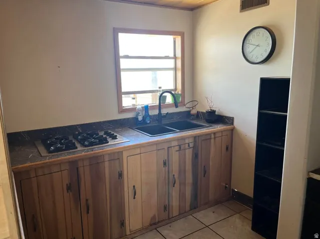Built-in gas stovetop, double basin sink with matte black faucet, wood-finish cabinetry, and patterned countertops