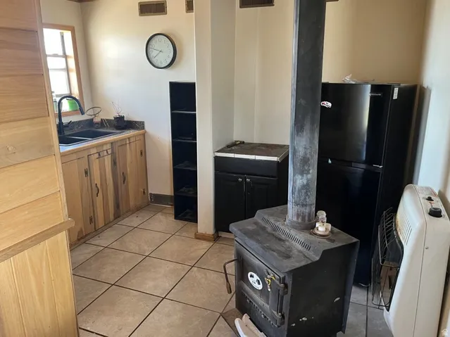 Tile flooring, wood-finish cabinetry, built-in sink with matte black faucet, and a freestanding wood-burning stove