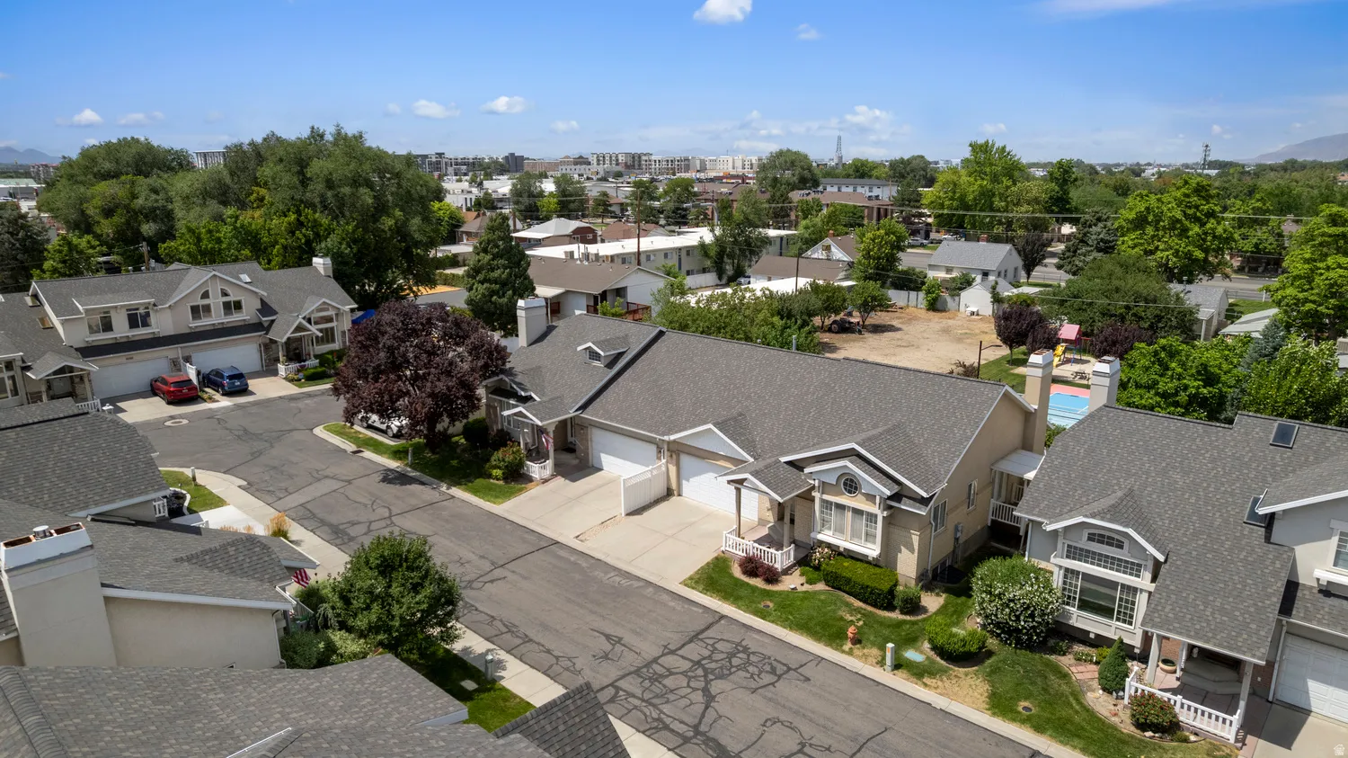Residential street featuring asphalt paving, mature trees, and a collection of properties with shingled roofs and attached garages
