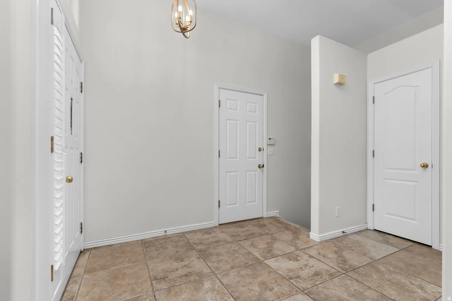 Entryway featuring large format tile flooring, vaulted ceiling, and white panel doors with brass hardware