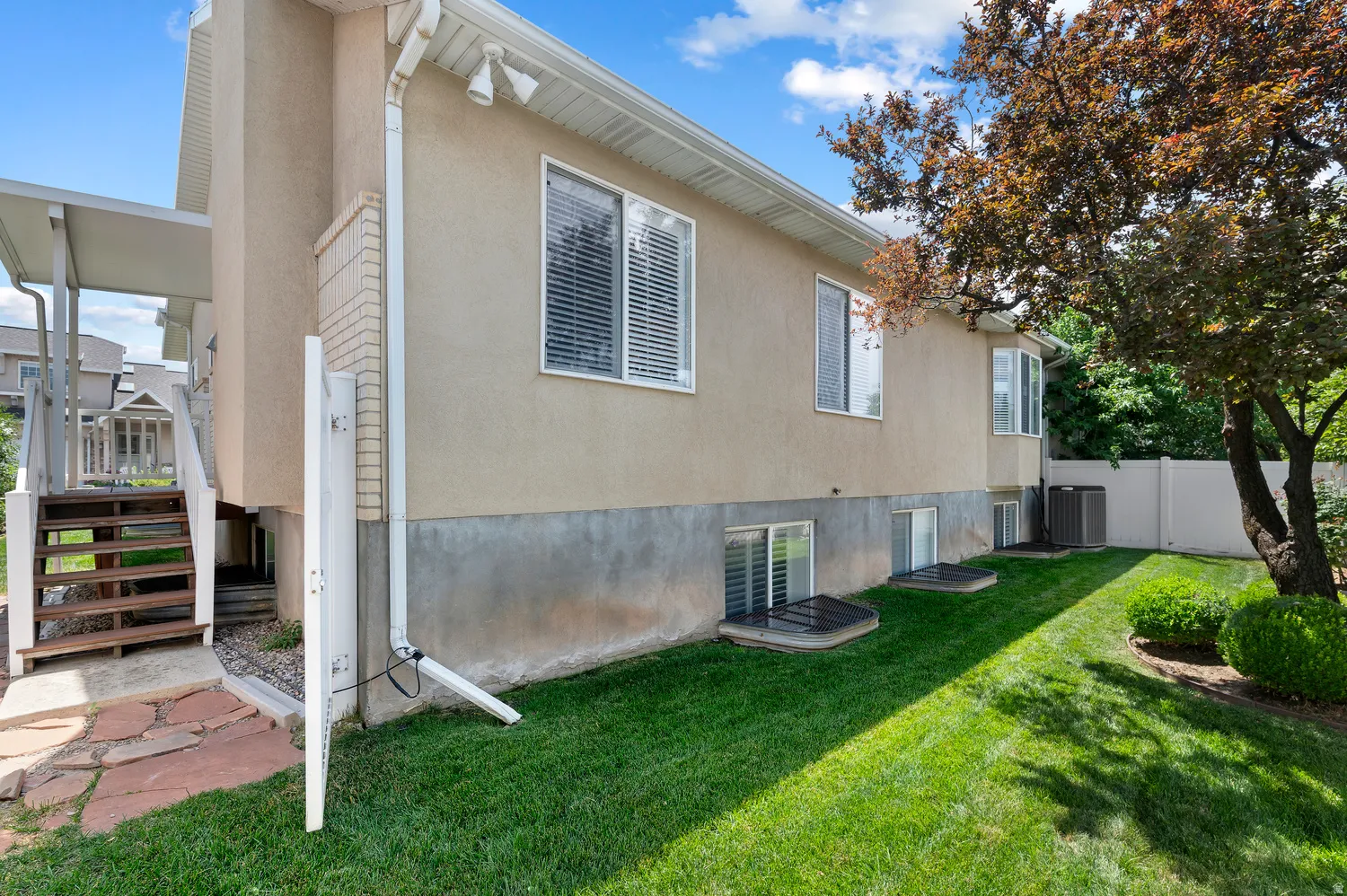Stucco exterior with multiple windows, a covered deck with stairs, a stone pathway, and a grassy lawn