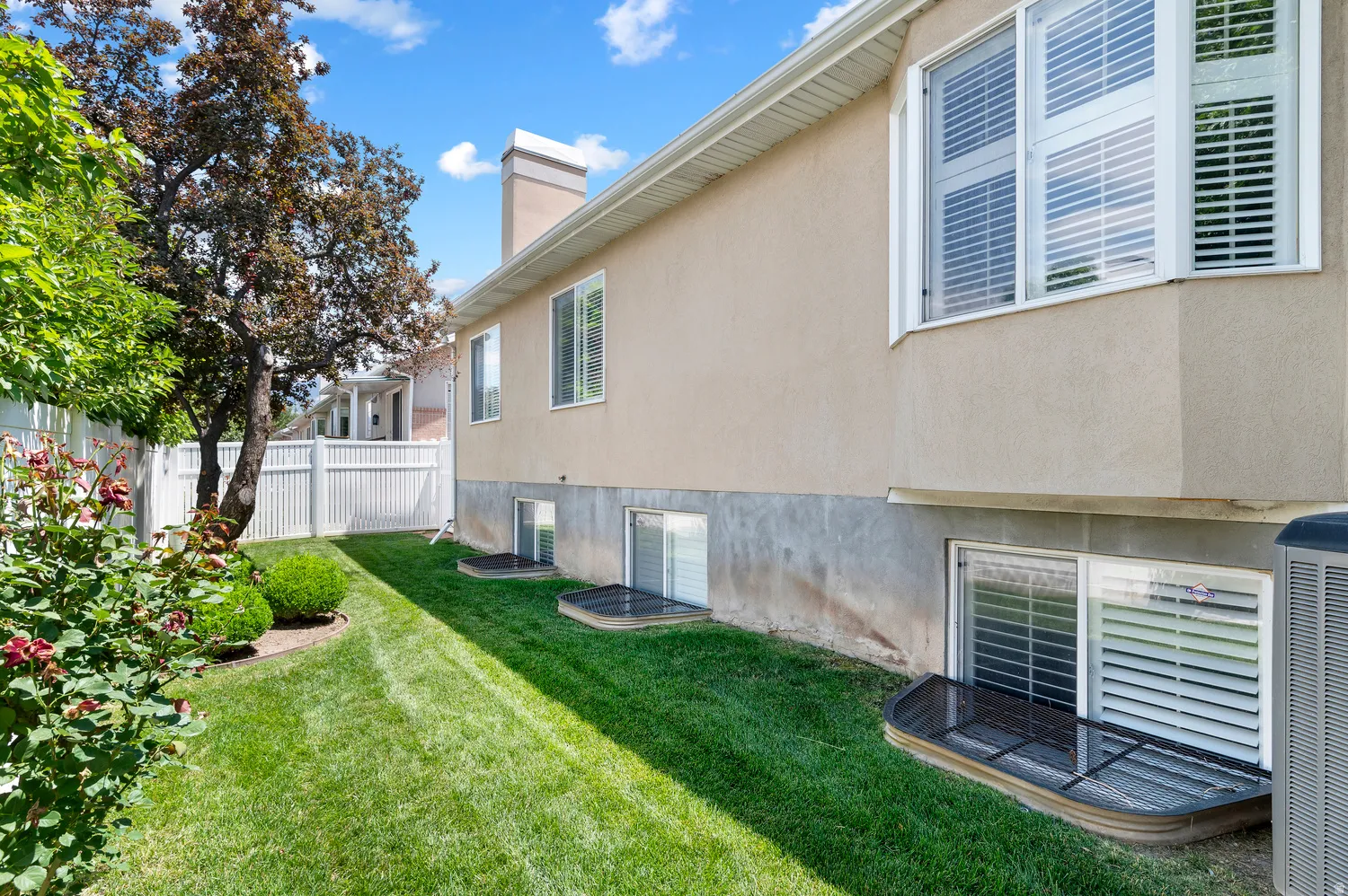 Side yard featuring a manicured lawn, established shrubbery, and a mature tree