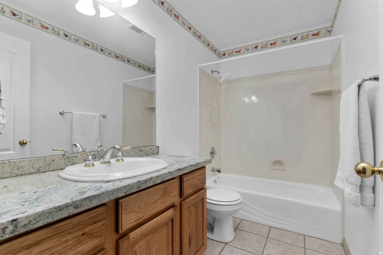 Bathroom featuring a vanity with a white oval sink, polished chrome faucet with brass accents, and a light-toned granite countertop