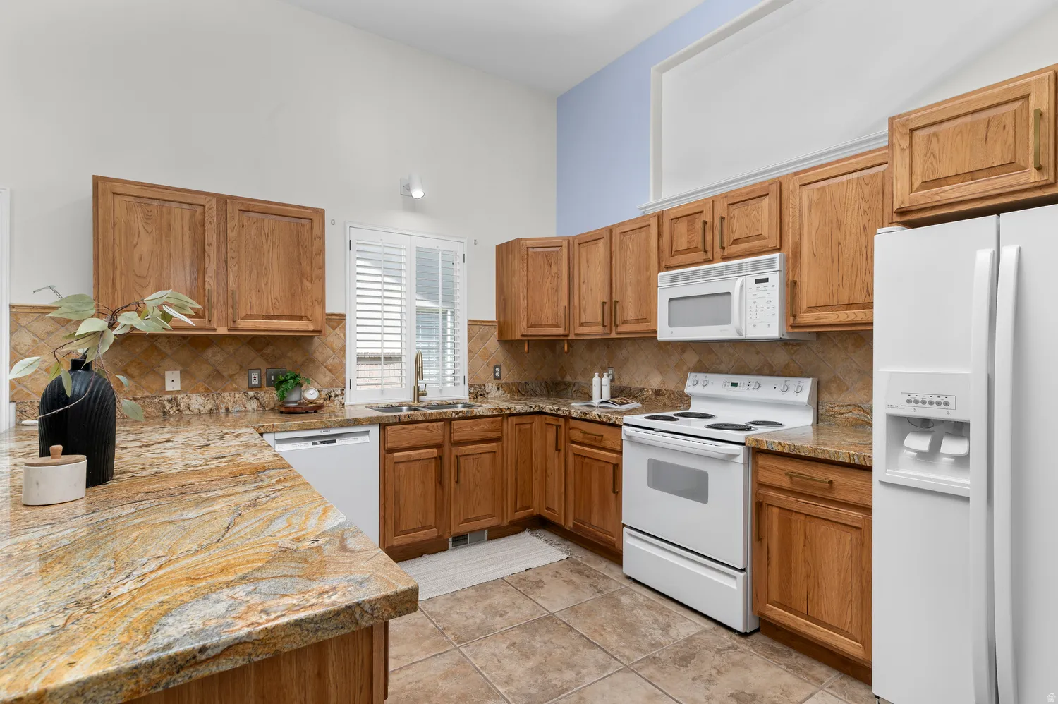 Kitchen featuring wood cabinetry, light-toned countertops, a tile backsplash, and white appliances