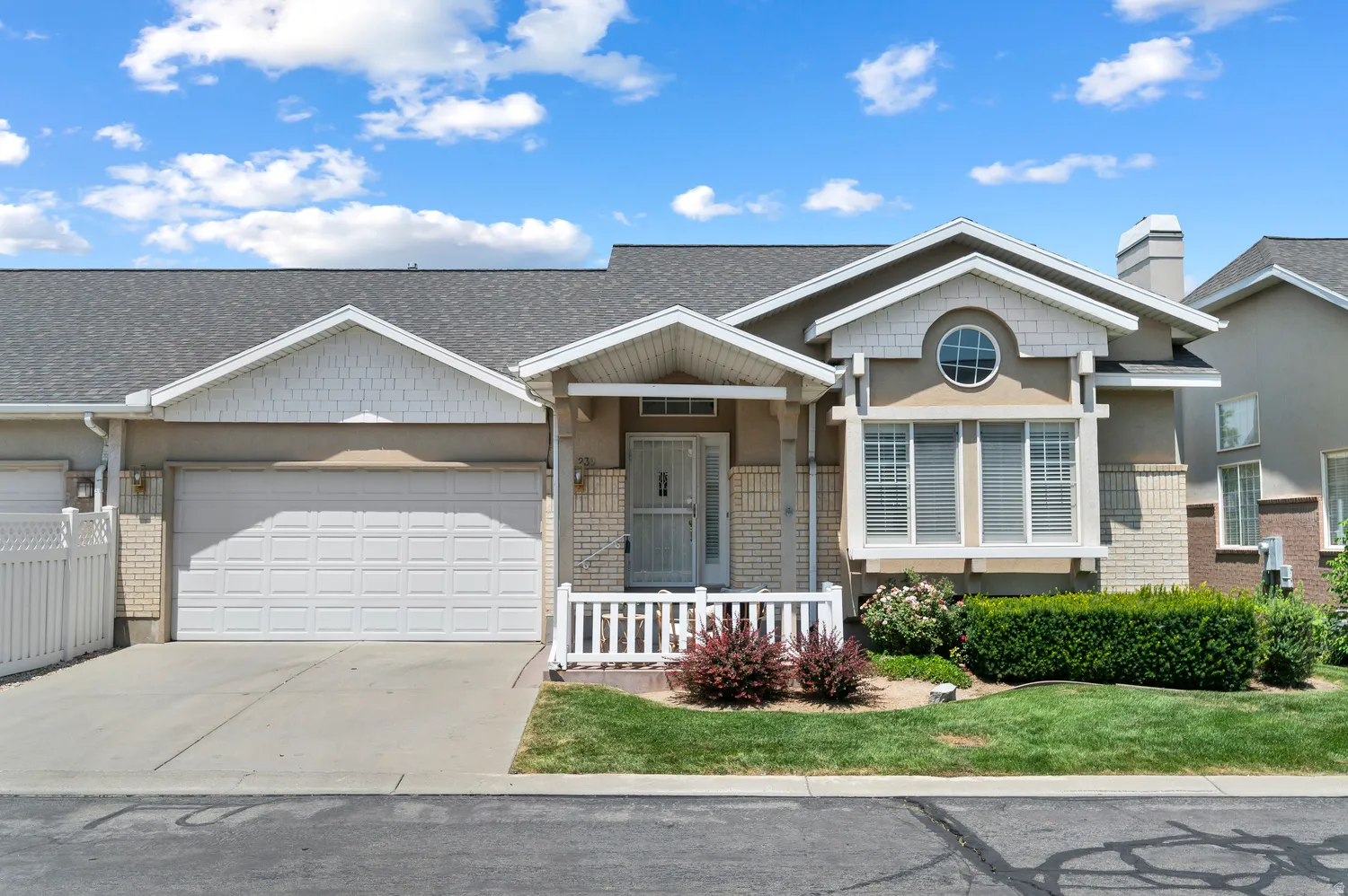 Exterior featuring stucco and light brick accents, a two-car garage, and a front porch with white railing