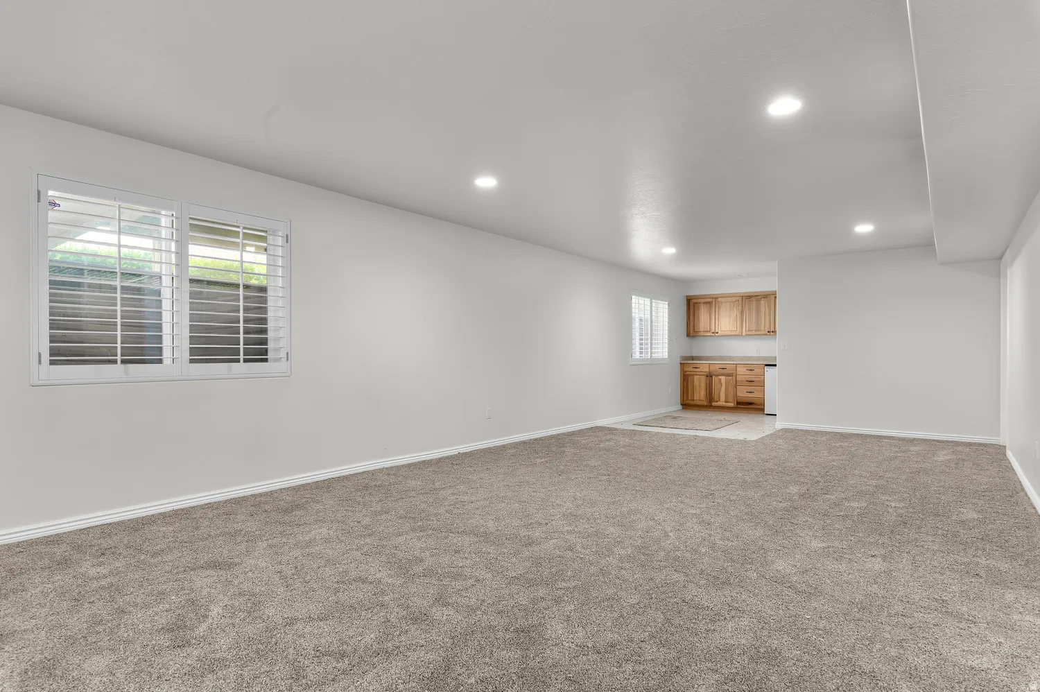Spacious room featuring new carpeting, recessed lighting, white walls, and white plantation shutters on the windows