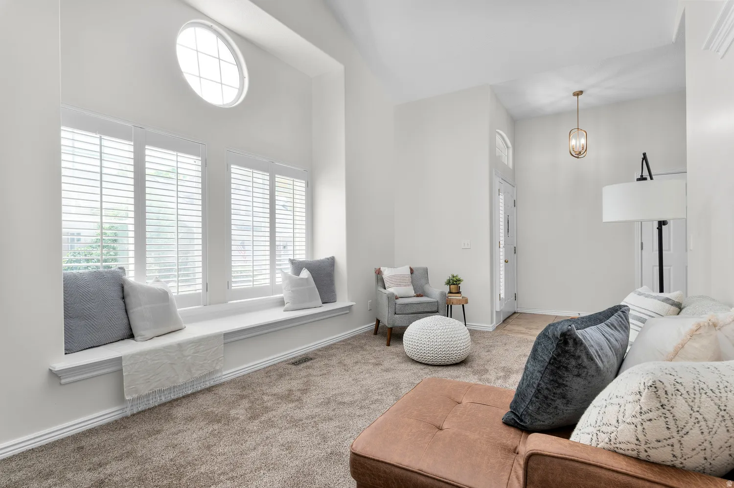 Vaulted ceiling living area featuring a prominent window seat, plantation shutters, an oval transom window, and a decorative pendant light fixture