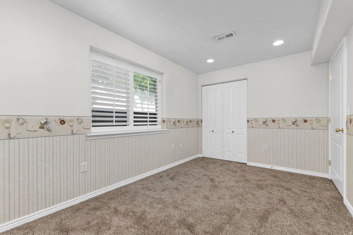 Carpeted interior room featuring a window with plantation shutters, recessed lighting, and white bi-fold closet doors