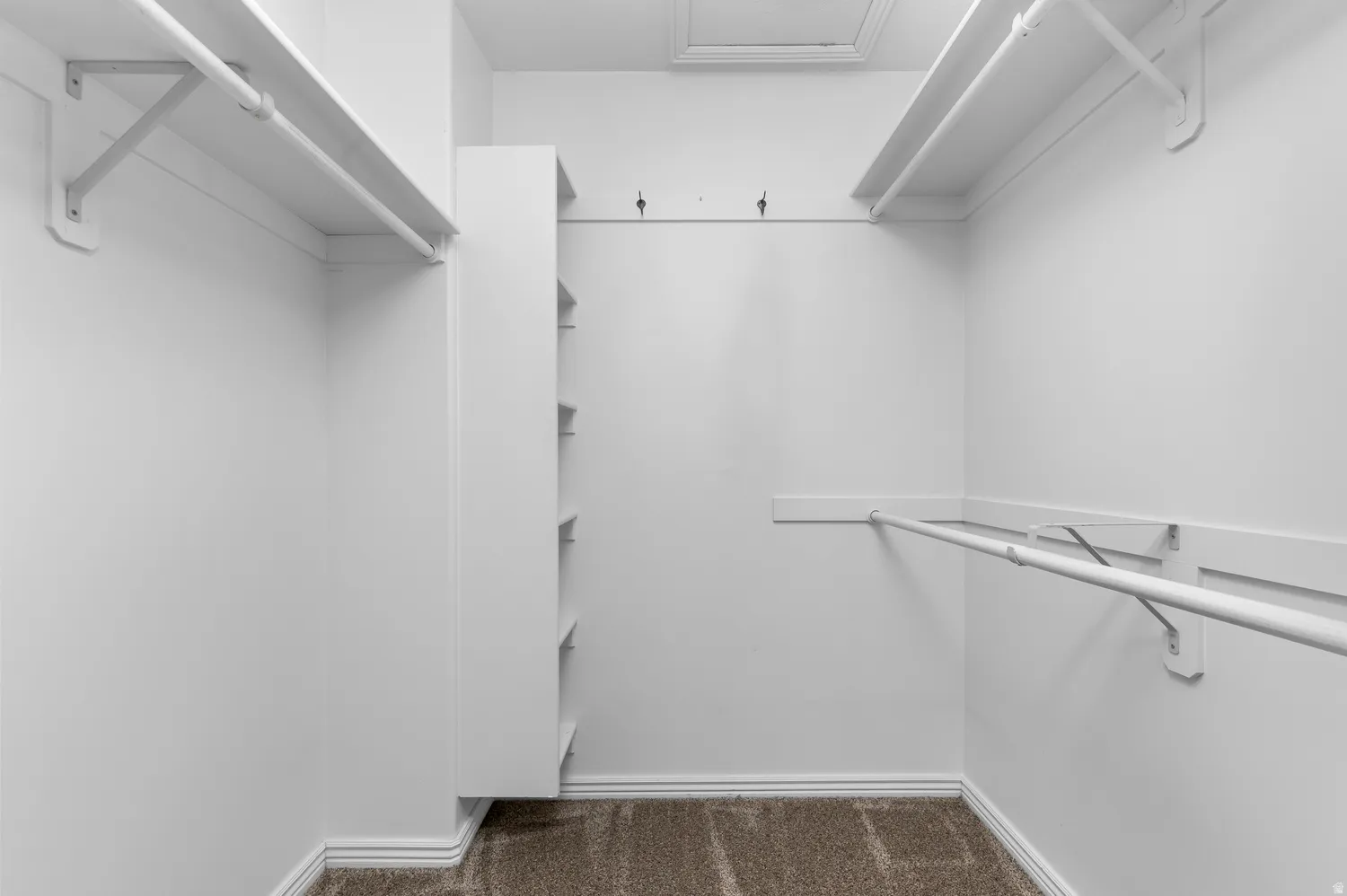 Primary Bedroom~Walk-in closet featuring built-in shelving, multiple hanging rods, wall-mounted hooks, and carpeted flooring