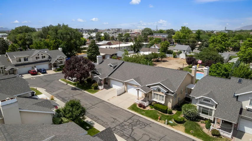 Residential street featuring asphalt paving, mature trees, and a collection of properties with shingled roofs and attached garages