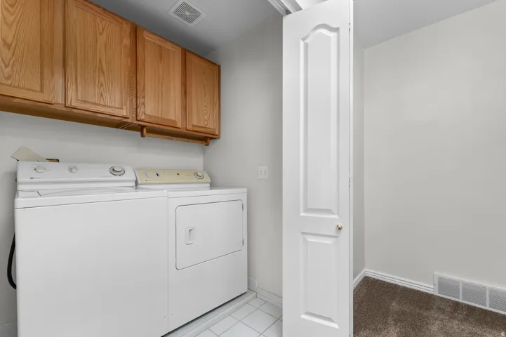 Utility area featuring overhead wood cabinetry and tile flooring