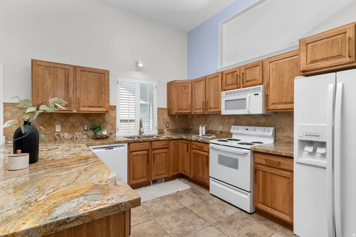 Kitchen featuring wood cabinetry, light-toned countertops, a tile backsplash, and white appliances