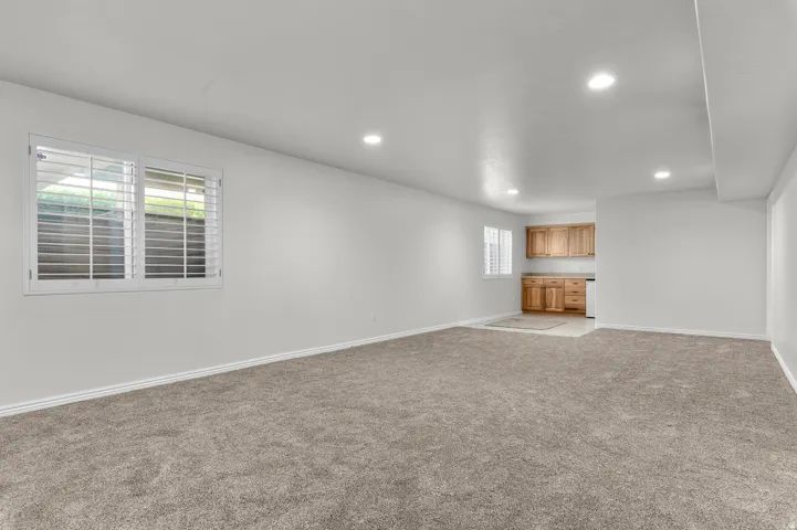 Spacious room featuring new carpeting, recessed lighting, white walls, and white plantation shutters on the windows