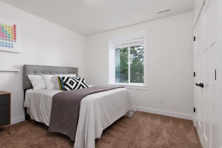 Bright room featuring a window with green foliage outside, neutral-toned carpet, white walls, and a white interior door with black hardware