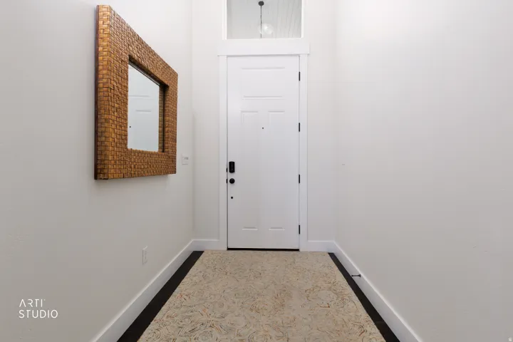 Entryway featuring a white paneled door with black hardware, a transom window, a decorative mirror with a textured frame, and a patterned floor runner